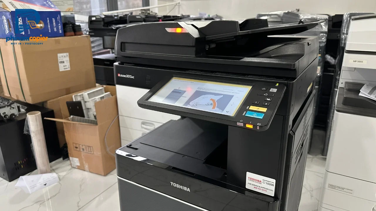 Máy photocopy Toshiba e-STUDIO3015AC mới trong kho, bên cạnh các thùng carton và thiết bị văn phòng khác.